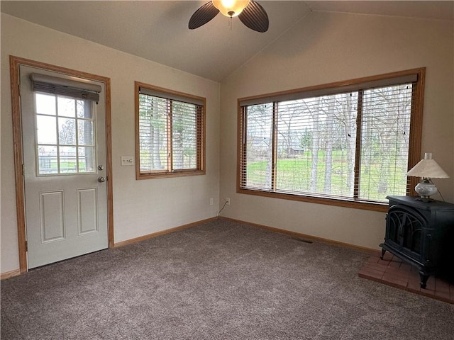 unfurnished living room featuring a healthy amount of sunlight, carpet floors, ceiling fan, and a wood stove