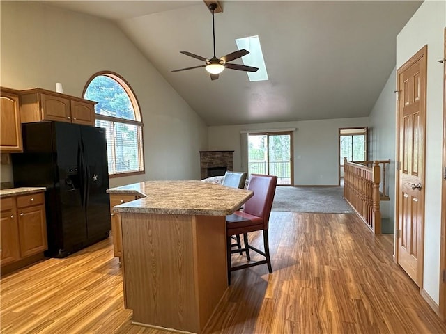 kitchen featuring ceiling fan, a skylight, a center island, black fridge with ice dispenser, and light wood-type flooring