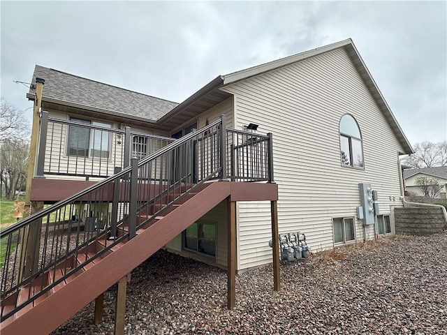 view of side of property featuring roof with shingles, a wooden deck, central AC unit, and stairway