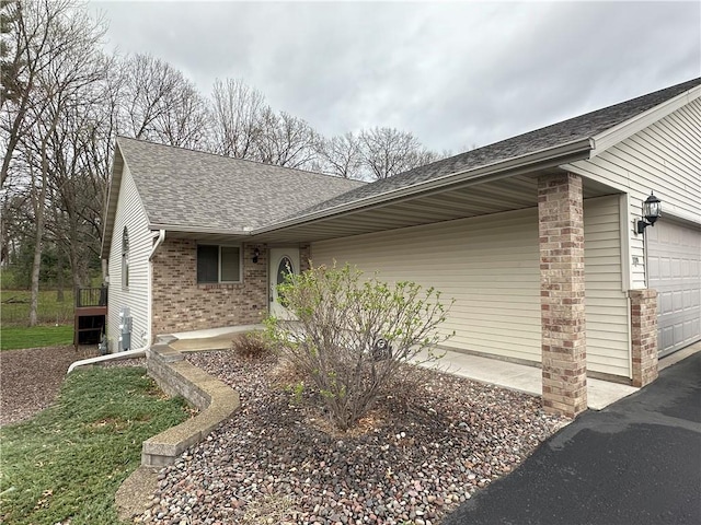view of side of property featuring brick siding, a garage, driveway, and a shingled roof