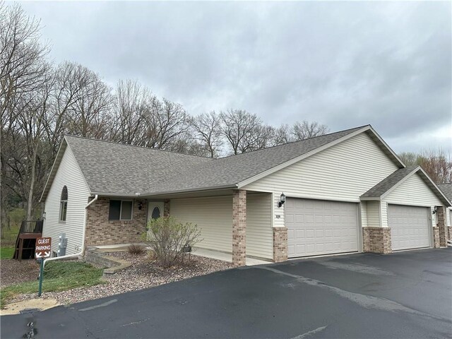 ranch-style home featuring brick siding, a garage, driveway, and a shingled roof