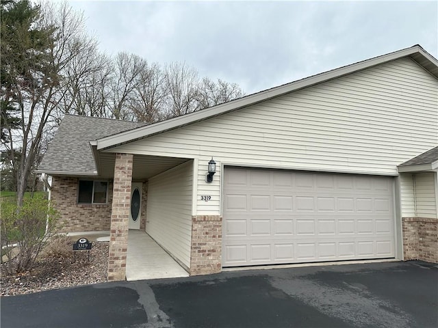 view of front of house featuring brick siding, a garage, aphalt driveway, and a shingled roof
