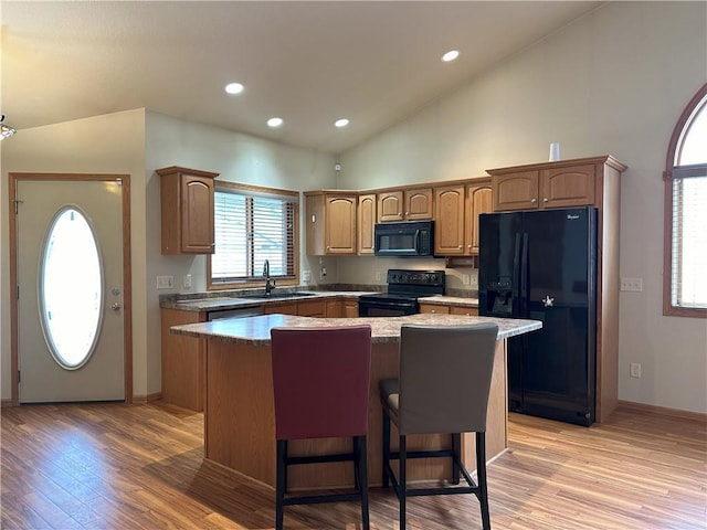 kitchen featuring a kitchen island, a breakfast bar, a sink, light wood-style flooring, and black appliances