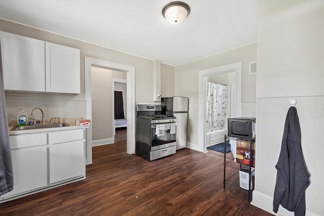 kitchen with freestanding refrigerator, dark wood-style floors, white cabinets, stainless steel range with gas stovetop, and a sink