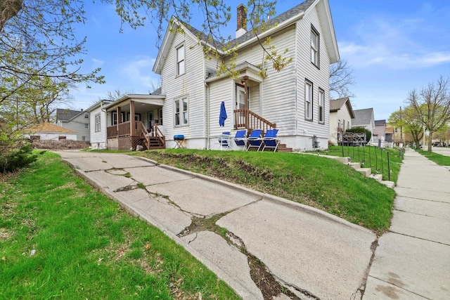 view of front of home with a front yard, a chimney, and covered porch