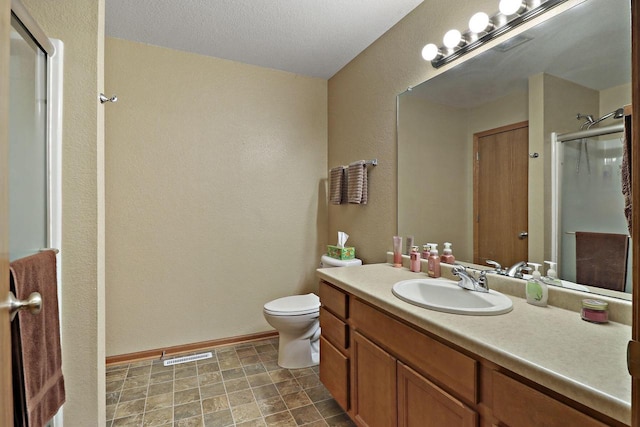 bathroom featuring visible vents, vanity, a textured wall, toilet, and a stall shower