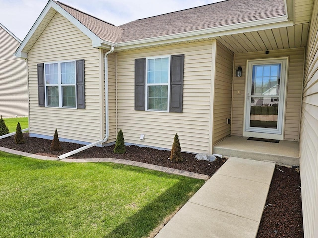 view of exterior entry with roof with shingles and a yard