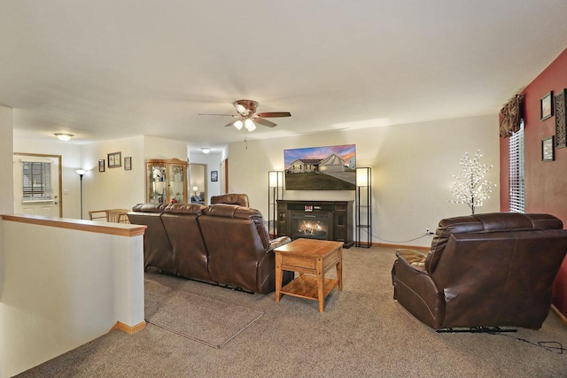 living room featuring a ceiling fan, a glass covered fireplace, and light carpet