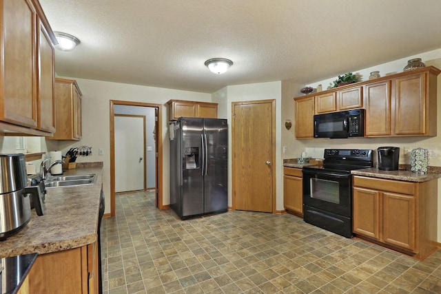 kitchen featuring brown cabinetry, a sink, a textured ceiling, and black appliances