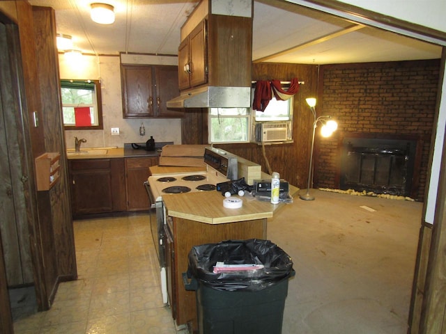kitchen with a sink, range with electric stovetop, light floors, under cabinet range hood, and a brick fireplace