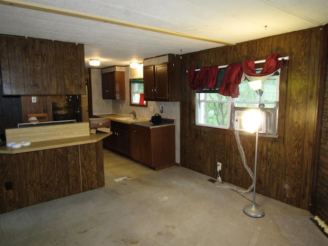 kitchen with dark brown cabinets, a sink, light colored carpet, light countertops, and wooden walls