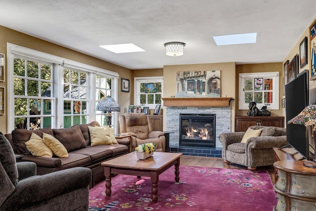 living area featuring wood finished floors, a skylight, and a stone fireplace