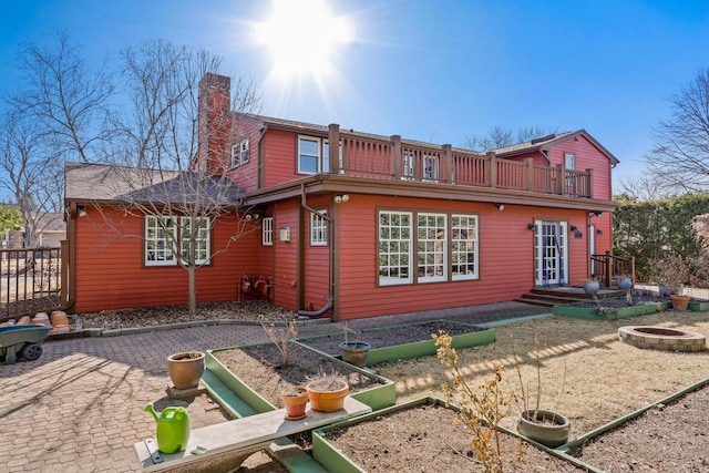 rear view of house featuring an outdoor fire pit, a chimney, a garden, a balcony, and a patio area