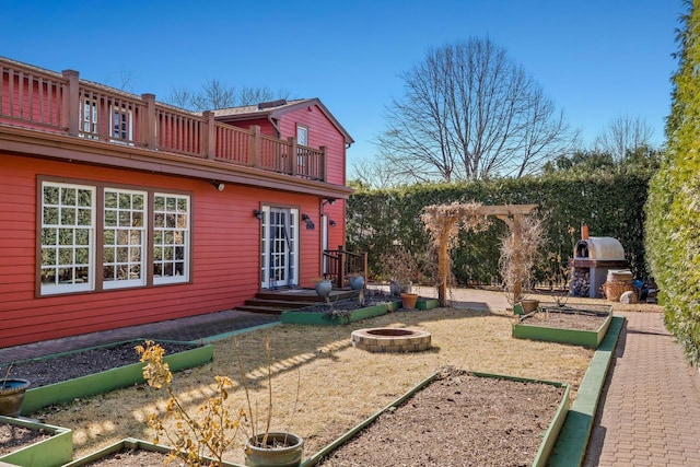rear view of property featuring an outdoor fire pit, a vegetable garden, and a balcony