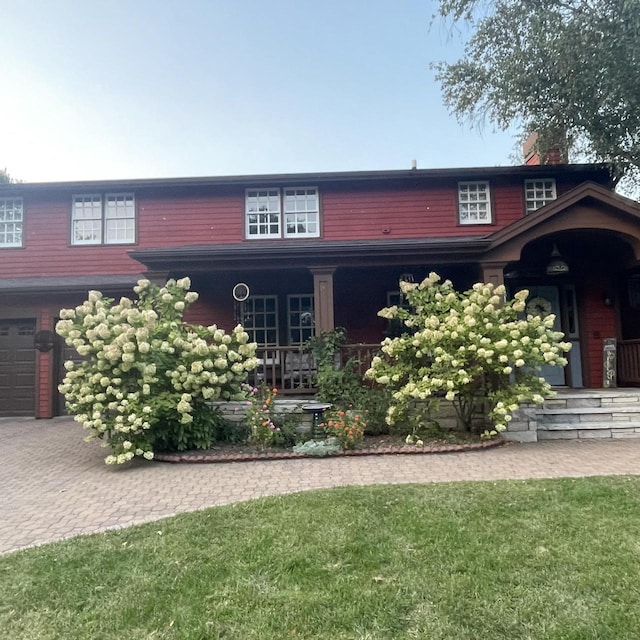 view of front of home with a chimney, a porch, a front lawn, and a garage
