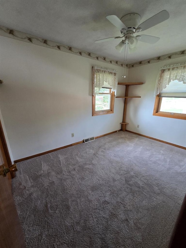 carpeted spare room with visible vents, baseboards, and ceiling fan