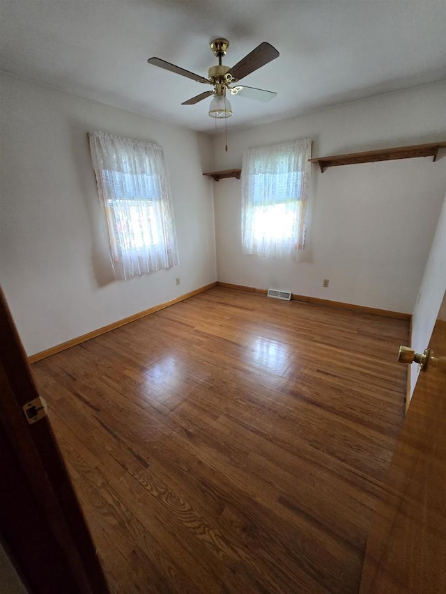 empty room with baseboards, ceiling fan, visible vents, and wood finished floors