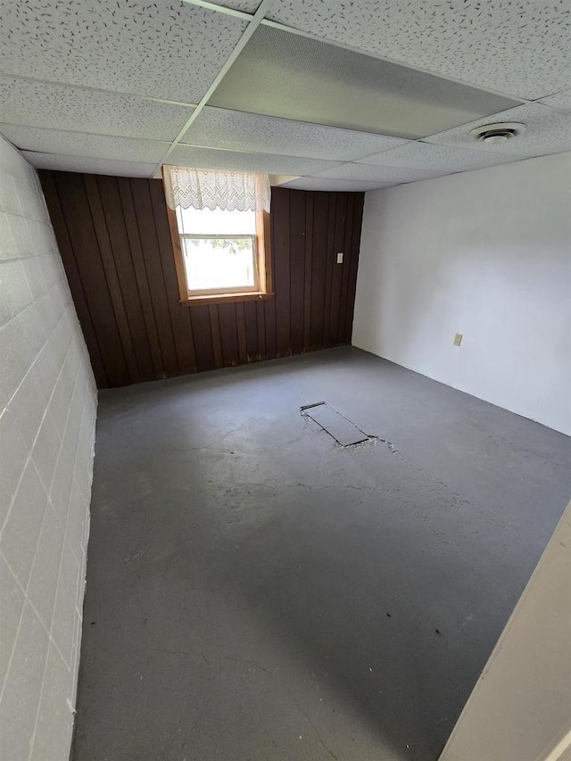 empty room with a paneled ceiling, wood walls, concrete floors, and concrete block wall