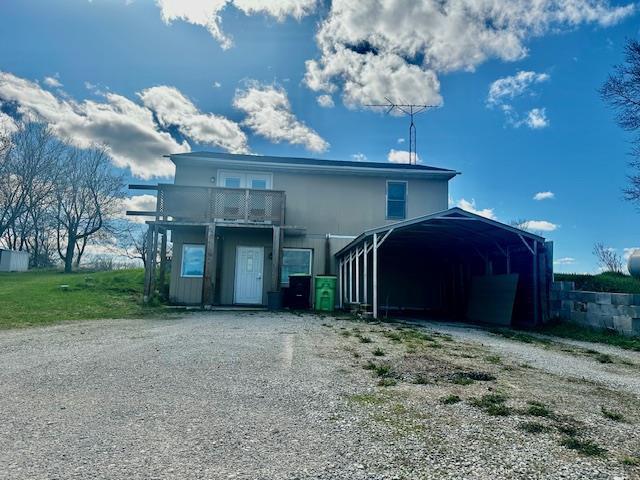 exterior space with dirt driveway, a balcony, and a carport