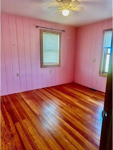 unfurnished room featuring wood walls, ceiling fan, and wood finished floors