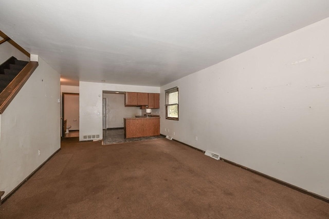 unfurnished living room with dark colored carpet, visible vents, baseboards, and stairs