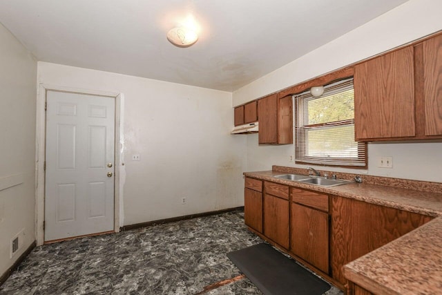 kitchen featuring under cabinet range hood, brown cabinetry, baseboards, visible vents, and a sink