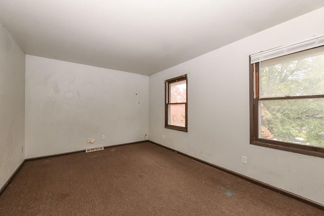 carpeted empty room featuring plenty of natural light, baseboards, and visible vents