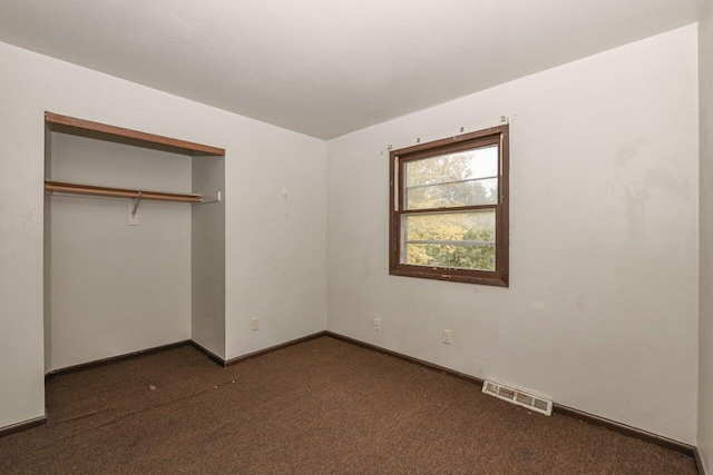unfurnished bedroom with a closet, visible vents, baseboards, and dark colored carpet