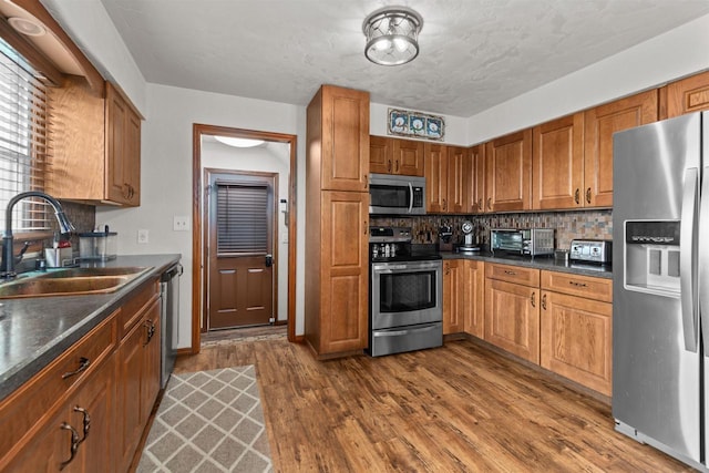 kitchen featuring brown cabinets, a sink, dark countertops, dark wood finished floors, and appliances with stainless steel finishes