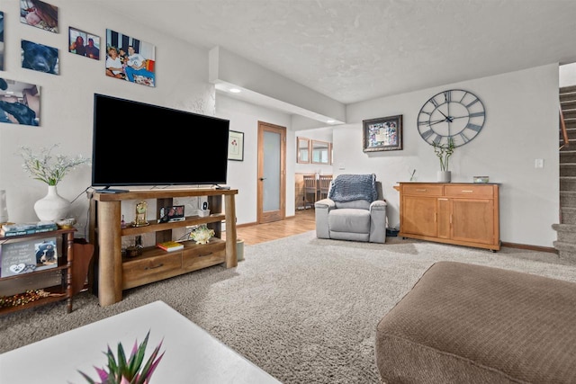 living area featuring stairway, a textured ceiling, carpet flooring, and baseboards