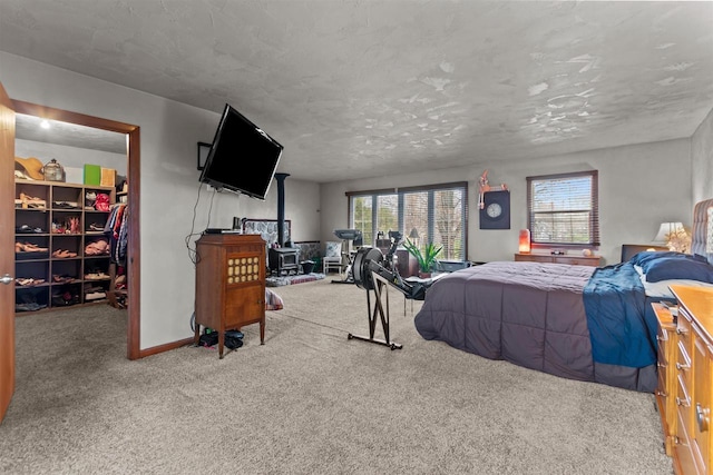 carpeted bedroom featuring a wood stove, a closet, baseboards, and a walk in closet