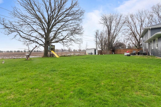 view of yard with a playground, an outdoor structure, fence, and a shed