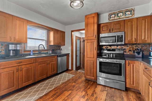 kitchen featuring brown cabinets, a sink, dark countertops, stainless steel appliances, and tasteful backsplash