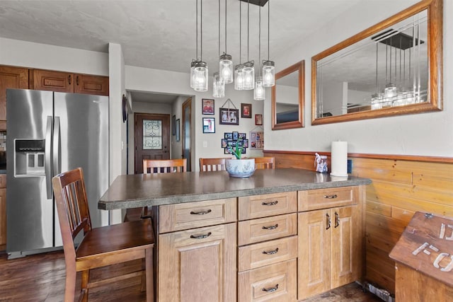 kitchen featuring a breakfast bar area, dark wood-style floors, hanging light fixtures, stainless steel fridge with ice dispenser, and dark countertops