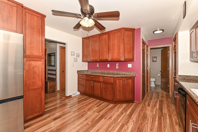kitchen with light wood finished floors, freestanding refrigerator, dark stone counters, brown cabinetry, and ceiling fan