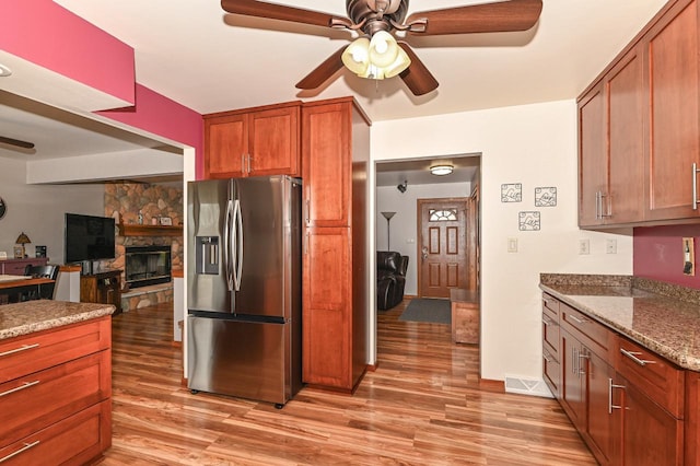 kitchen with brown cabinets, light wood-style flooring, a ceiling fan, stainless steel fridge with ice dispenser, and a stone fireplace