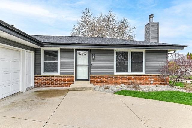 view of exterior entry featuring a shingled roof, a chimney, and brick siding