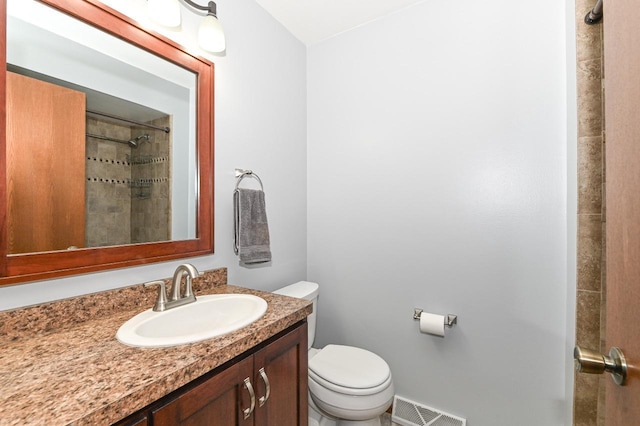 full bath featuring vanity, toilet, tiled shower, and visible vents