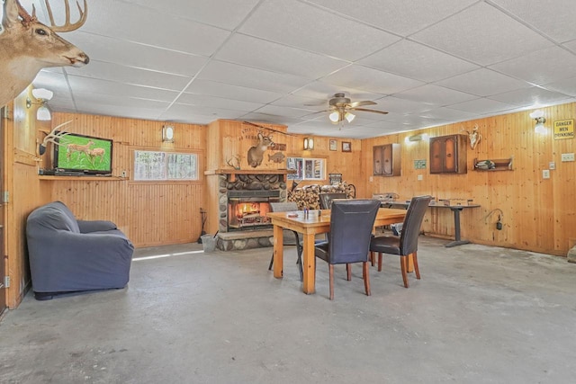 7589 Nose Lake Rd, Rhinelander, WI 54501 - dining space with a paneled ceiling, wood walls, concrete flooring, a stone fireplace, and ceiling fan