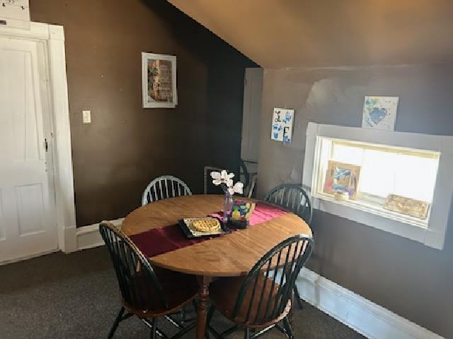 carpeted dining area featuring baseboards and vaulted ceiling
