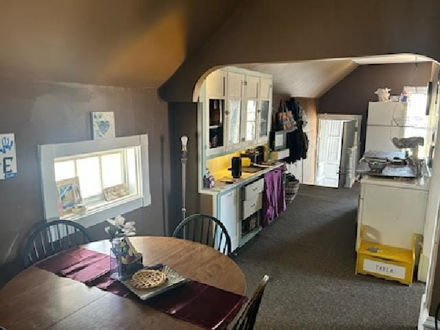 dining room with lofted ceiling, dark colored carpet, and arched walkways