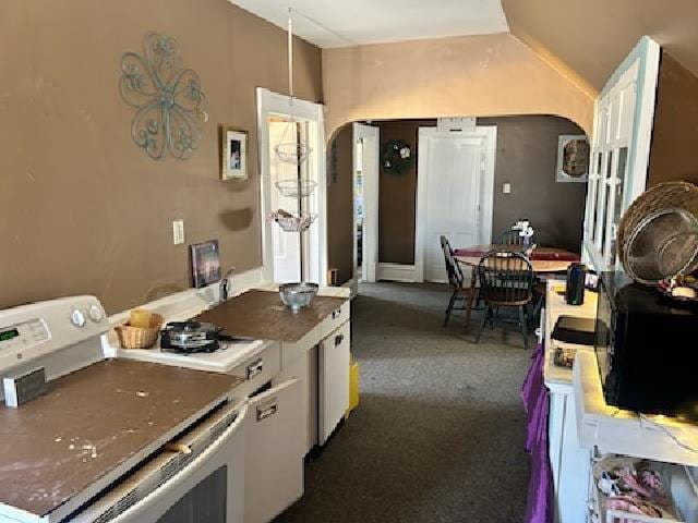 kitchen featuring vaulted ceiling, white range with electric stovetop, dark colored carpet, and arched walkways