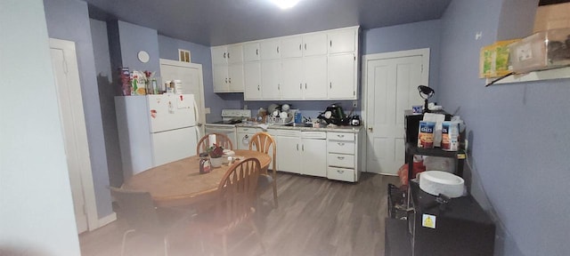 kitchen featuring white cabinets, light countertops, wood finished floors, and white appliances