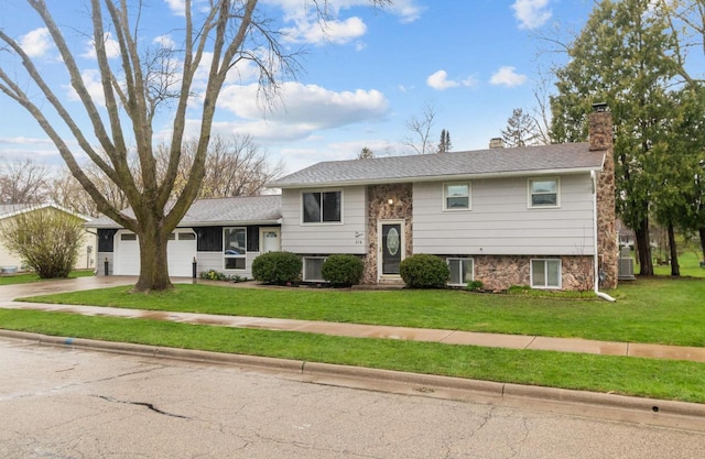split foyer home featuring a front lawn, concrete driveway, a chimney, and a garage