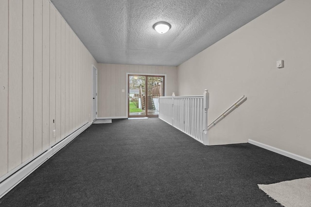 unfurnished room with a textured ceiling, wooden walls, baseboards, and dark carpet