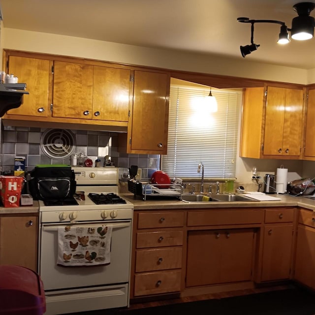 kitchen with white range with gas stovetop, a sink, brown cabinetry, light countertops, and tasteful backsplash
