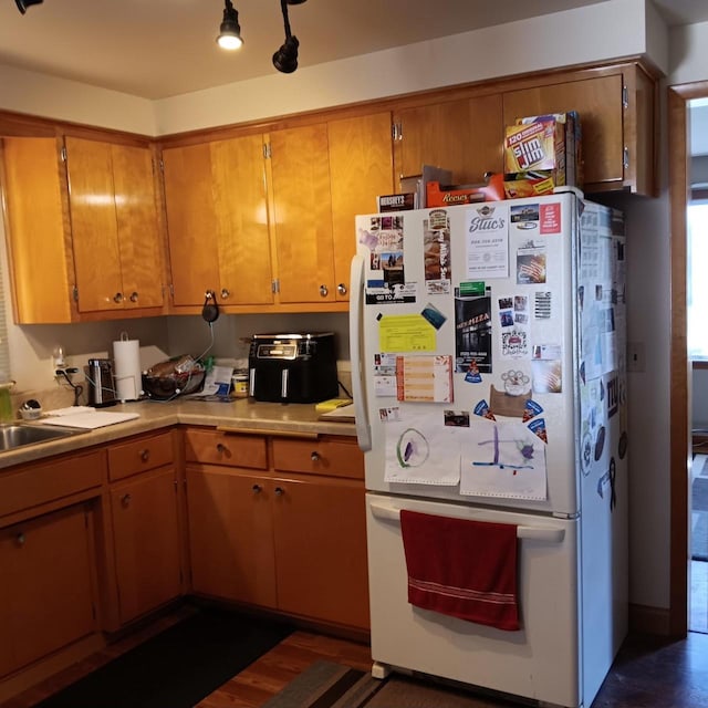 kitchen with a sink, freestanding refrigerator, light countertops, and brown cabinets