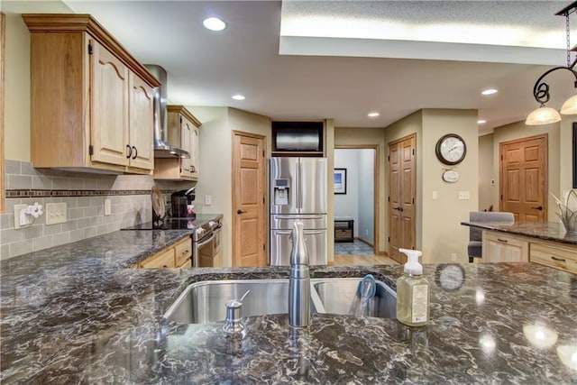 kitchen featuring a sink, dark stone counters, wall chimney exhaust hood, stainless steel appliances, and tasteful backsplash