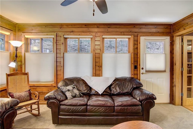 carpeted living room with wooden walls, a ceiling fan, and a healthy amount of sunlight