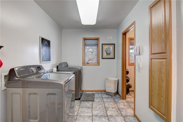 clothes washing area with laundry area, baseboards, stone finish floor, and washer and dryer